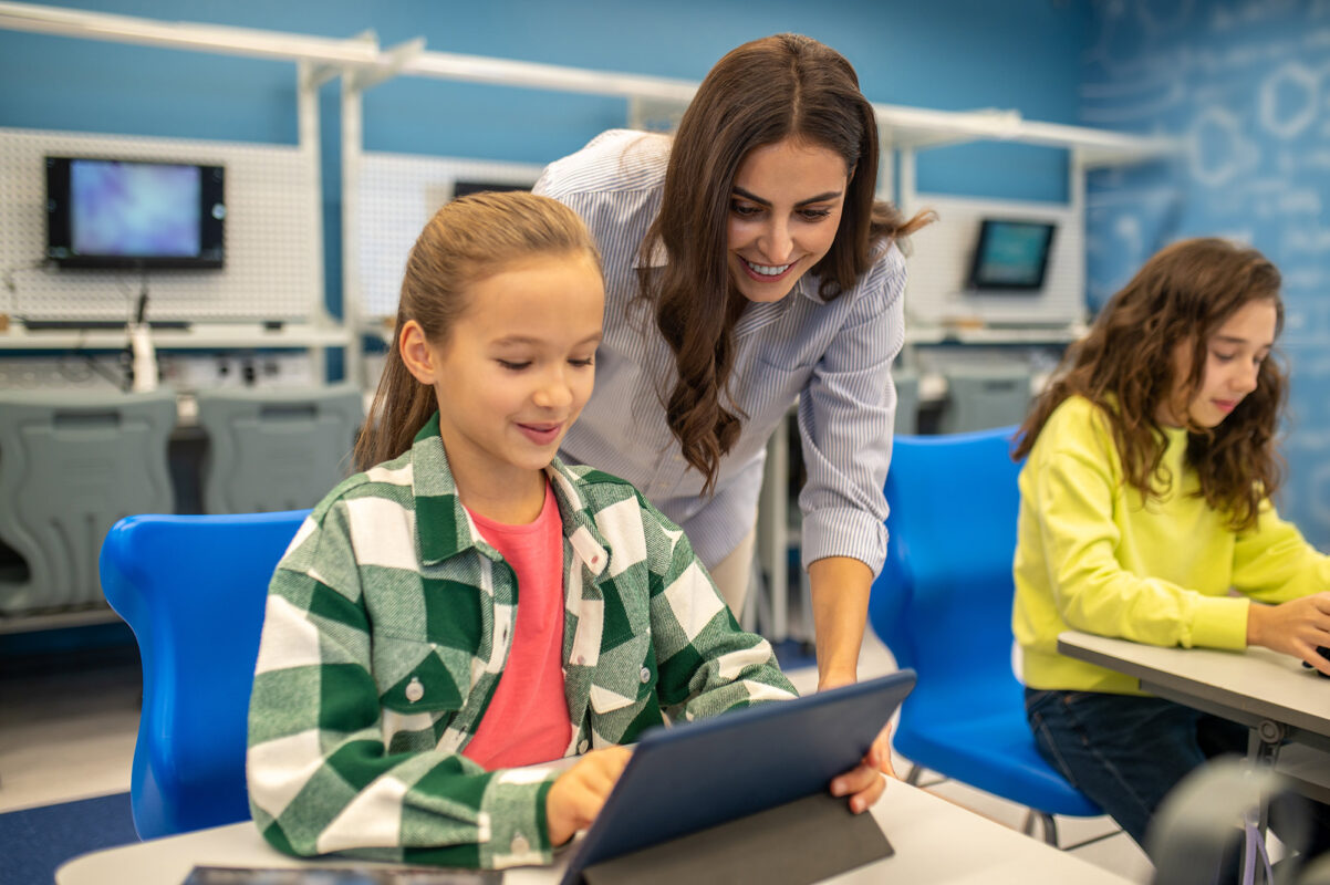 Girl in classroom with teacher looking at a tablet